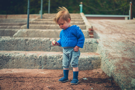 Little toddler eating banana on steps outside