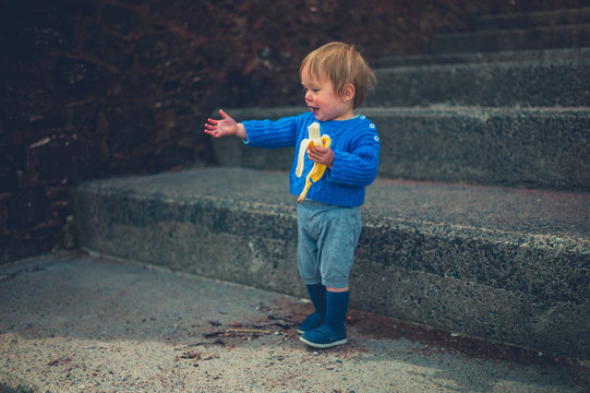 Little toddler eating banana on steps outside