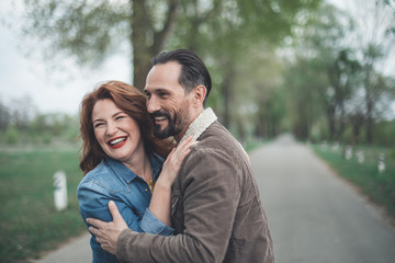 Fototapeta premium Waist up portrait of glad mature loving couple enjoying date in the nature. They are cuddling and smiling with happiness 