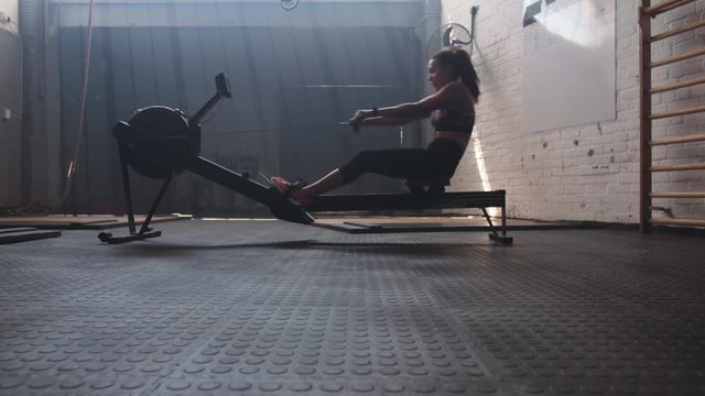Shot of a strong young woman exercising with rowing machine gym. Female athlete training in gym.
