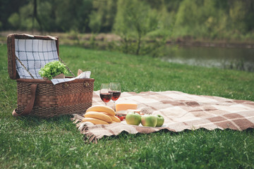 Everything for romantic picnic. Healthy food and glasses of wine on blanket. Picnic basket is on...