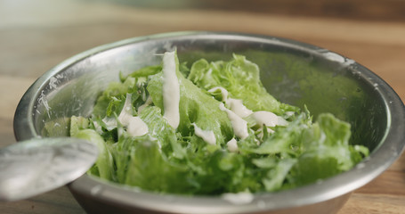 closeup mixing frillis salad leaves with caesar sauce