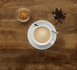 A cup of Cappuccino on antique wood, with coffee beans.