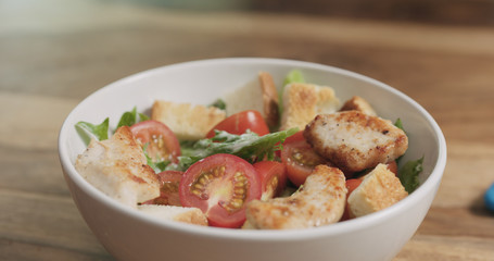 closeup adding chicken to caesar salad