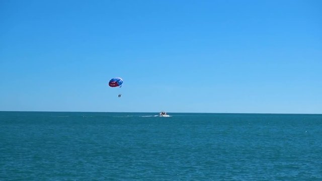 a colored parachute hovers in the sky attached to the boat. in the open sea against the blue sky in good weather. sea parasailing