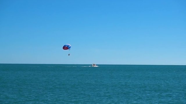 a colored parachute hovers in the sky attached to the boat. in the open sea against the blue sky in good weather. sea parasailing