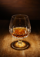 A spotlight on a single crystal glass of brandy, shot on a wooden table top.