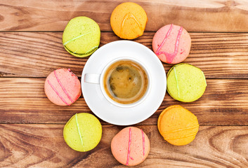 Cup of coffee with colorful macaroons on the wooden table. Top view.
