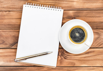 Blank notepad with pen and cup of coffee on the table. Top view.