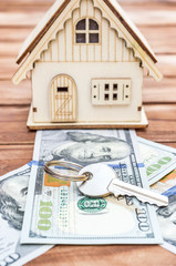 Model of house with dollar bills and key on wooden background.