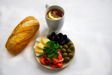 Breakfast - black tea with lemon, bread, and plate with red fish, olives and cheese