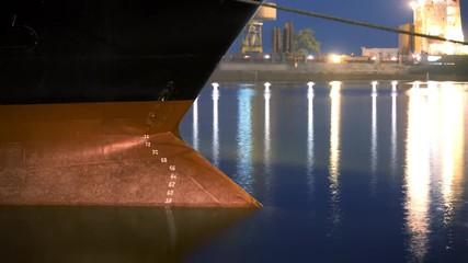 Day to night timelapse of submerged under the cargo weight freighter bow of ship into the water. Draft marks on a bulker - waterline numbers on bow and stern of a vessel at seaport in the evening