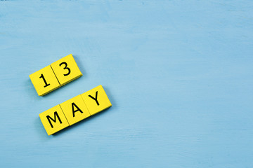 MAY 13, yellow cube calendar on blue wooden surface with copy space