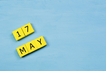 MAY 17, yellow cube calendar on blue wooden surface with copy space