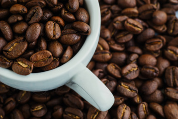 Fried brown coffee beans in a white cup.