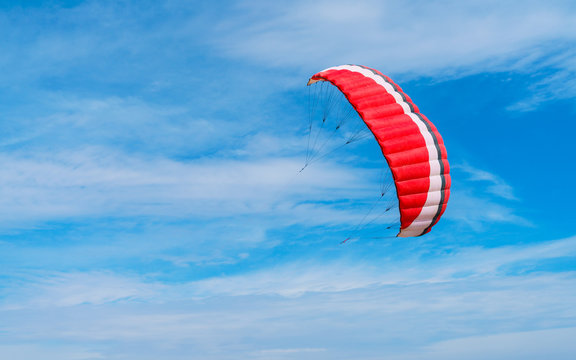 Bright scarlet or red wing parachute with white and black stripes against blue sky with feathery clouds