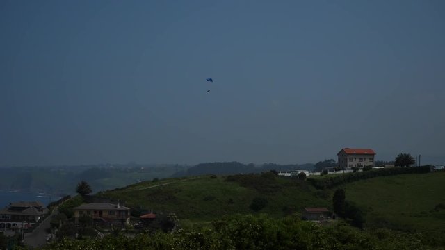 paraplane flying over the green hill near the ocean in the countryside