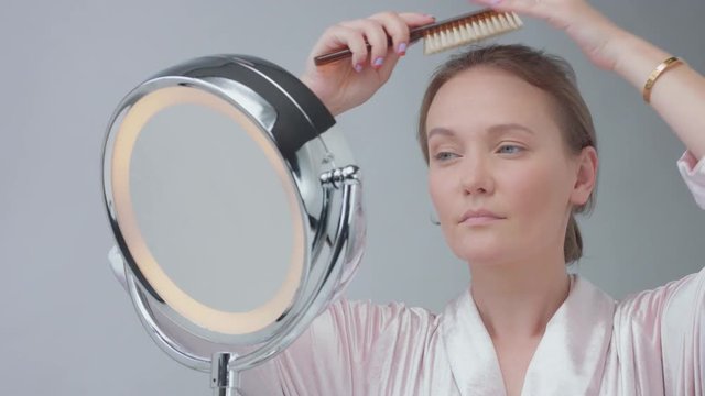 young blue eyed caucasian woman looking at mirror and combing her hair