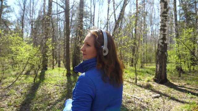 A young girl in the Park listening to music in headphones. A woman walks through the spring Park and enjoy the music.