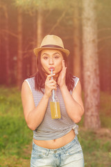 Young woman outdoors on sunny summer day drinking lemonade from the bottle. Natural lighting, no retouch, hazy filter.