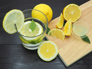 Fresh lemon juice in small bowl and lemon slice on dark wood background