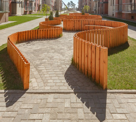 The walking area is surrounded by a decorative wooden fence of curved shape. Paved with tiles of different shapes.