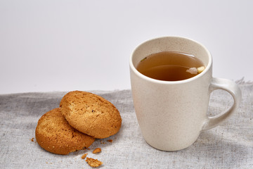 White porcelain mug of tea and sweet cookies on homespun napkin over white background, top view, selective focus