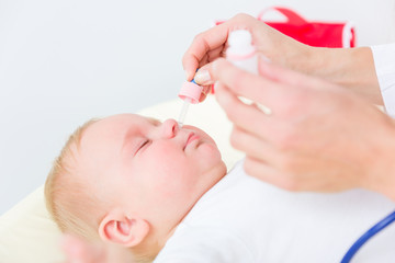 Close-up of the hands of a pediatrician clearing the nose of a baby, by applying saline solution in the nostrils with a nasal aspirator during physical check-up