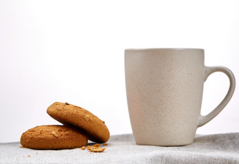 White porcelain mug of tea and sweet cookies on homespun napkin over white background, top view, selective focus