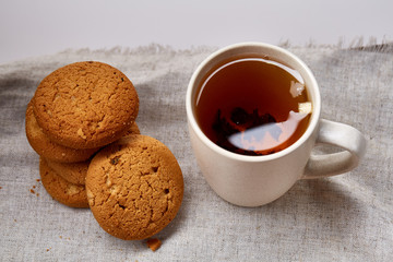 White porcelain mug of tea and sweet cookies on homespun napkin over white background, top view, selective focus