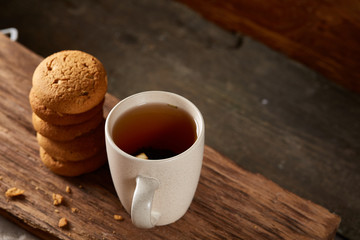 White porcelain mug of tea and sweet cookies on piece of wood over wooden background, top view, selective focus