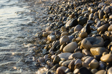 pebble stones on the sea beach, the rolling waves of the sea with foam