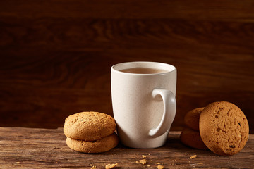 White porcelain mug of tea and sweet cookies on piece of wood over wooden background, top view, selective focus