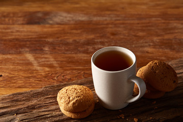 White porcelain mug of tea and sweet cookies on piece of wood over wooden background, top view, selective focus