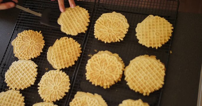 A handheld overhead shot of a woman placing freshly-baked pizzelles on a cooling sheet.  	