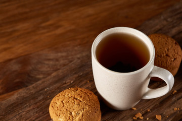 White porcelain mug of tea and sweet cookies on piece of wood over wooden background, top view, selective focus