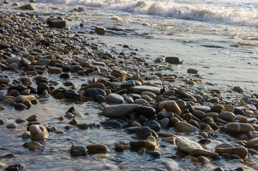 pebble stones on the sea beach, the rolling waves of the sea with foam