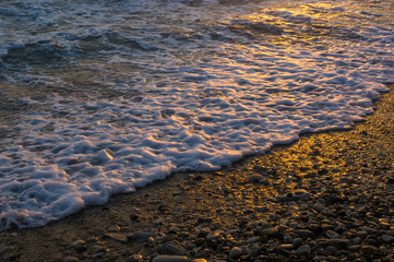 Amazing sea sunset on the pebble beach, the sun, waves, clouds