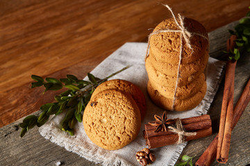 Christmas composition with pile of cookies, cinnamon and dried oranges on light wooden background, close-up.
