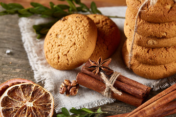 Christmas composition with pile of cookies, cinnamon and dried oranges on light wooden background, close-up.