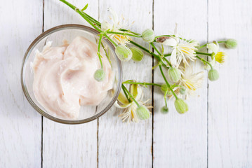 Fototapeta na wymiar cosmetic cream and white wildflower on bright wood table background