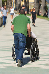 Obraz na płótnie Canvas Man pushes disabled in wheeled chair