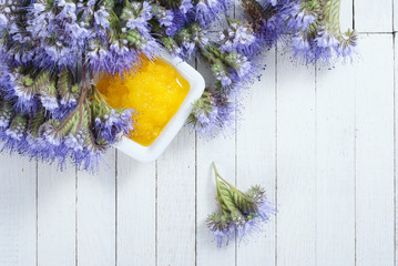 crystallized phacelia honey and flowers on white wooden background