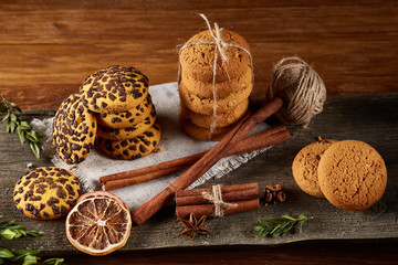 Christmas composition with pile of cookies, cinnamon and dried oranges on wooden background, close-up.