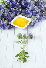 crystallized phacelia honey and flowers on white wooden background