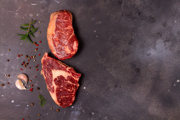 Raw beef steak with spices on dark stone background, top view scene with copy space