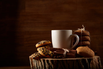 Christmas concept with a cup of hot tea, cookies and decorations on a log over wooden background, selective focus
