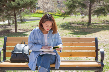 Student reading book and sitting on the bench in an university campus