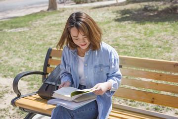 Student reading book and sitting on the bench in an university campus