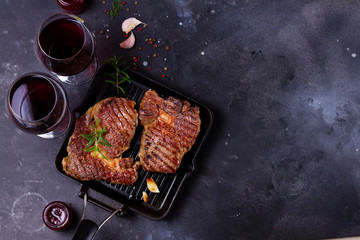 Hot Grilled beef steak on dark background with two glasses of red wine with copy space